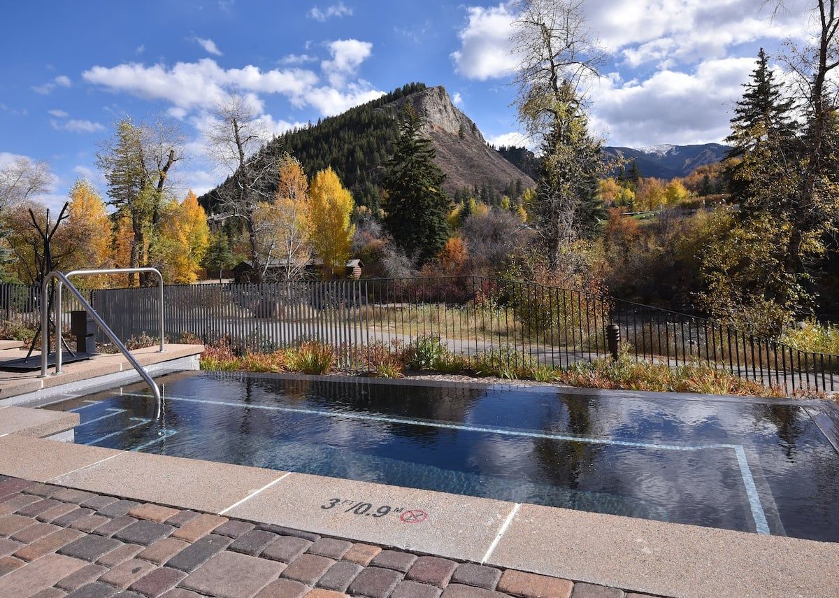 Une piscine extérieure avec vue sur les montagnes, entourée d’arbres et d’une clôture.