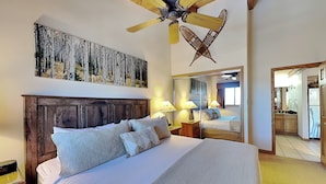 A bedroom with a wooden headboard, a large bed with multiple pillows, a ceiling fan, a wall-mounted painting, and a mirror reflecting the room. - 🌲Timberline C3B Deluxe 1-Bedroom + Loft ~Hot Tub~Pool~WiFi~Ski-in/out~Local Shuttle🌲 (Snowmass Village)
