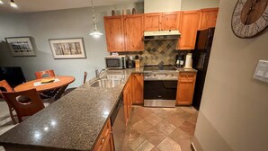A kitchen with granite countertops, wooden cabinets, a stainless steel sink, a microwave, a stove, and a clock on the wall. - Glacier Lodge - Deluxe Ski in/Ski out (Whistler)