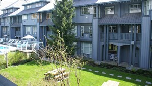 A multi-story hotel with a pool area, outdoor seating, and a well-maintained lawn. - Glacier Lodge - Deluxe Ski in/Ski out (Whistler)