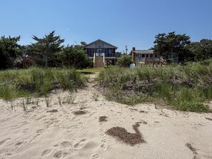 A beachfront property with a large house, a wooden deck, and a sandy path leading to the entrance. - Isle Of Skye:  Sandy sound side beach, excellent for water activities. (Ocracoke)