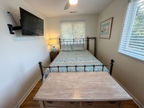A bedroom with a bed, bedside lamp, TV, and a window with blinds. - Isle Of Skye: Sandy sound side beach, excellent for water activities. (Ocracoke)