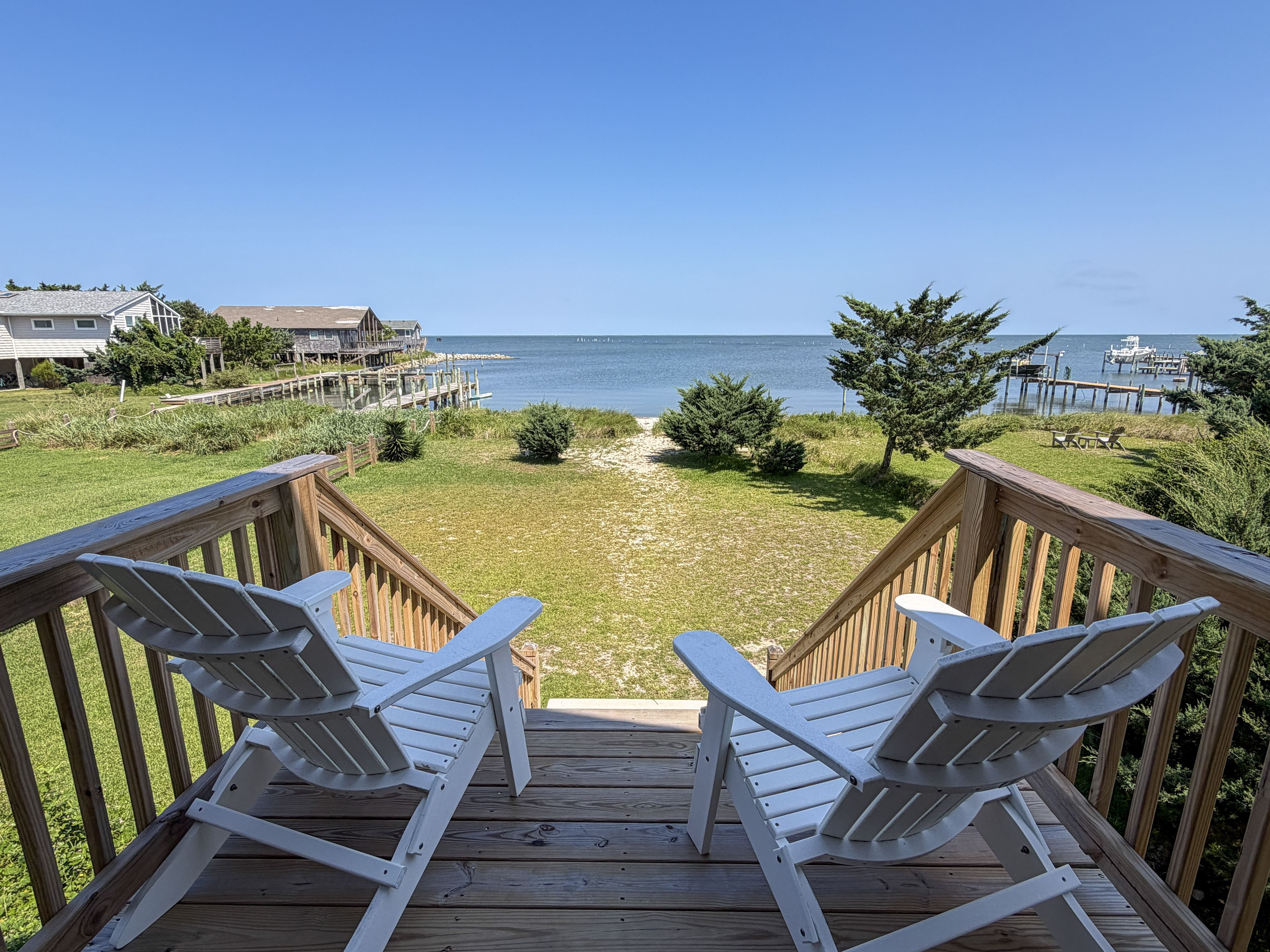 A wooden deck with two Adirondack chairs facing a beach and ocean view.