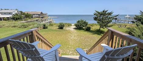 A wooden deck with two Adirondack chairs facing a beach and ocean view.