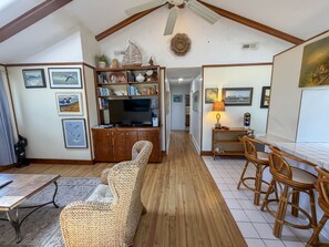 A spacious living area with a high ceiling, wooden flooring, a wicker sofa, a dining table with chairs, and a television on a wooden cabinet. - Isle Of Skye:  Sandy sound side beach, excellent for water activities. (Ocracoke)