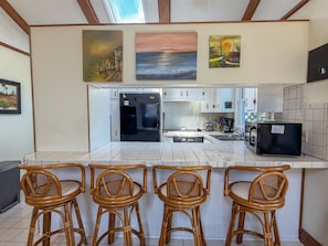 A kitchen with a central island, four wicker chairs, and three paintings on the wall. - Isle Of Skye: Sandy sound side beach, excellent for water activities. (Ocracoke)