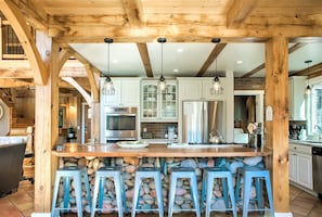 A kitchen with a stone countertop, bar stools, and modern appliances. - Pine Hollow | Mountain Lodge Near Asheville | Pool, Hot Tub, Fire Pit, Game Room | Event-Friendly (Fairview)