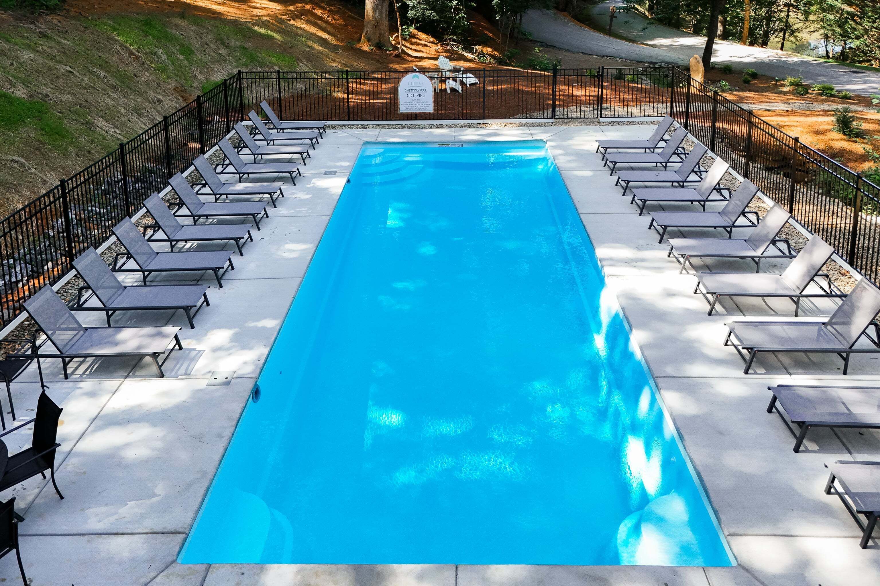 A rectangular swimming pool with lounge chairs on both sides, surrounded by a black fence, and a sign indicating no diving.