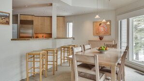A modern kitchen with wooden cabinets, a stainless steel refrigerator, and a dining area with a wooden table and chairs. - Ski Storage, Garage and Free Shuttle (Warm Springs)