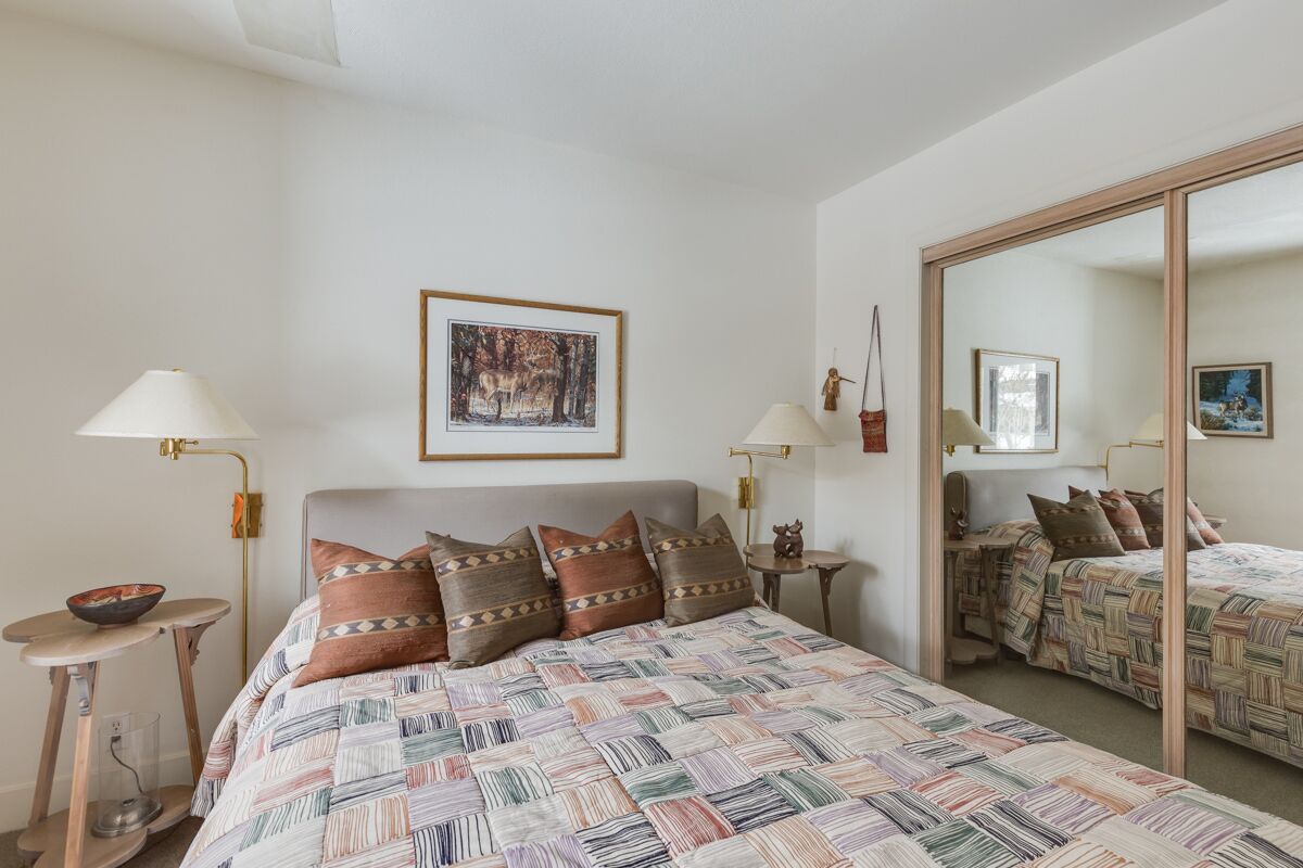 A bedroom with a large bed, two bedside tables, a mirror, and a framed picture on the wall.