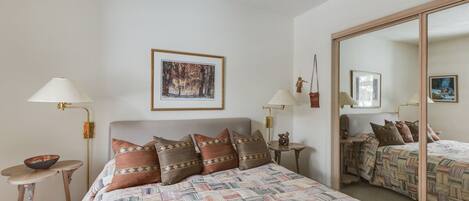 A bedroom with a large bed, two bedside tables, a mirror, and a framed picture on the wall.