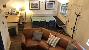 A cozy living room with a brown leather couch, a dining table with chairs, and a kitchen area in the background. - Iconic Sun Valley - Parkside Village - Sleeps 7 very comfortably  (Ketchum)