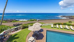 Un espace aménagé au bord de la piscine, avec vue sur l’océan, comprenant un barbecue et des chaises longues.
