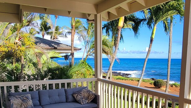 Un balcon avec un canapé et une petite table, donnant sur une plage bordée de palmiers et sur l’océan.