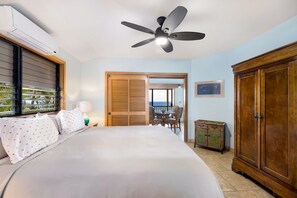 Une chambre d’hôtel avec un lit, un ventilateur de plafond, une vue sur l’océan, une porte en bois et un placard.