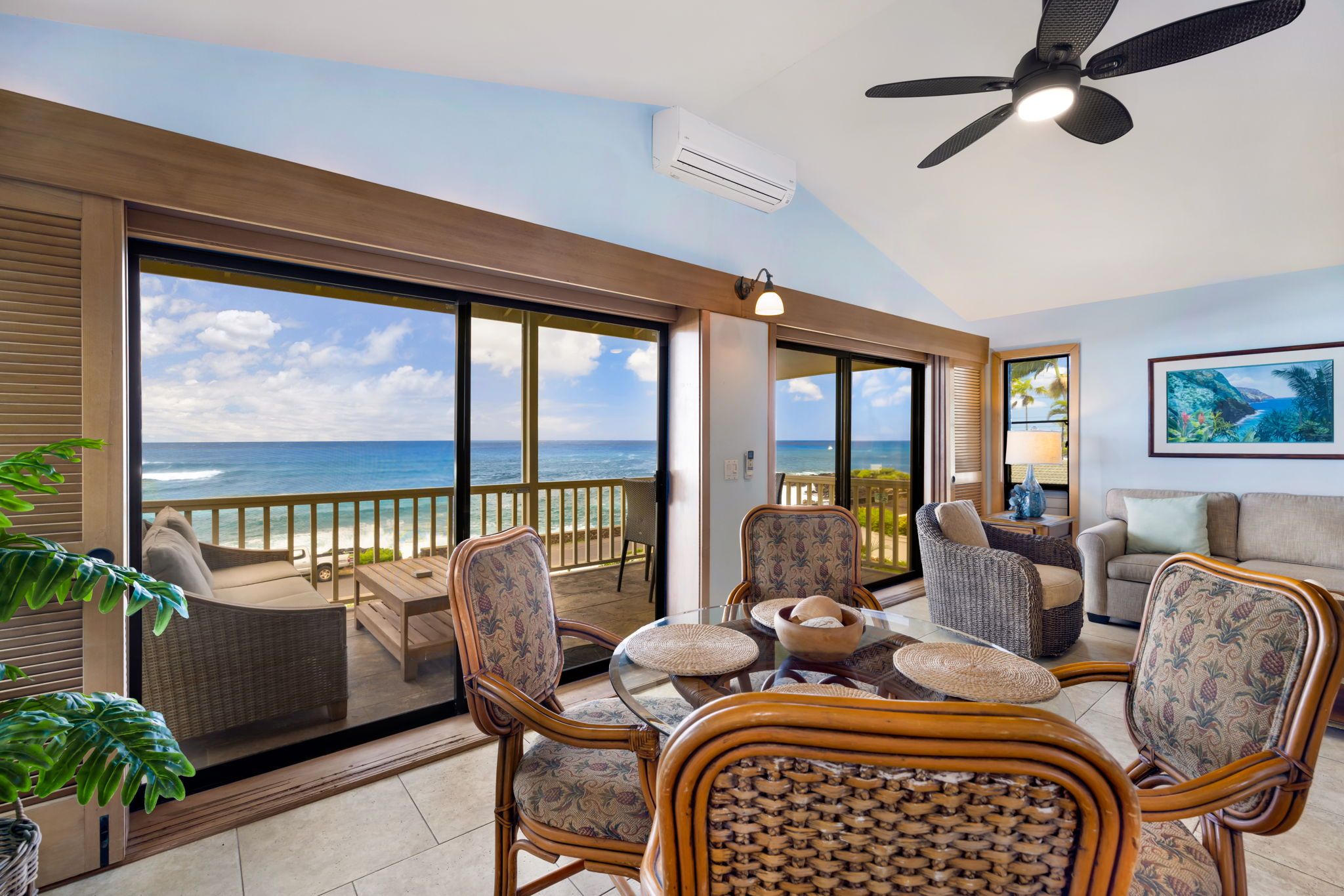 A spacious balcony with a view of the ocean, furnished with wicker chairs and a table, and a ceiling fan.