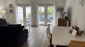 A living room with a sofa, a dining table, and a view through glass doors to an outdoor area with chairs. - Spacious, Pet Friendly, Townhome short walk to the beach with backyard (New Smyrna Beach)