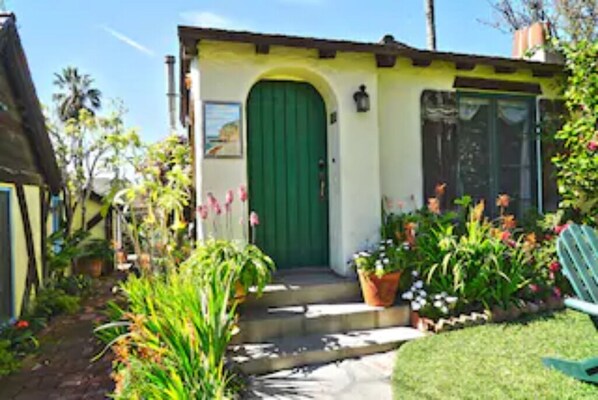 A small, single-story building with a green door and a small porch area.