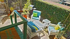 Un espace extérieur aménagé en terrasse, avec des meubles en osier, notamment un canapé et des fauteuils, une petite table et une structure décorative en bois.