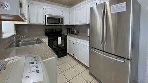 Una cocina moderna con armarios blancos, electrodomésticos de acero inoxidable, incluyendo un refrigerador y microondas, un horno empotrado y una cafetera.
