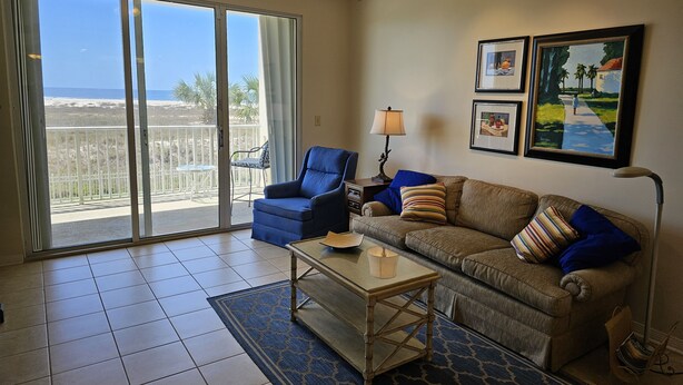 A living room with a sofa, armchair, and a coffee table. There is a balcony with a view of the beach. - Inn at Dauphin Island 211 Beautiful Views!! (Dauphin Island)