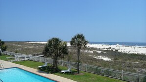 A pool area with lounge chairs, a fenced beach view, and a clear sky. - Inn at Dauphin Island 211 Beautiful Views!! (Dauphin Island)