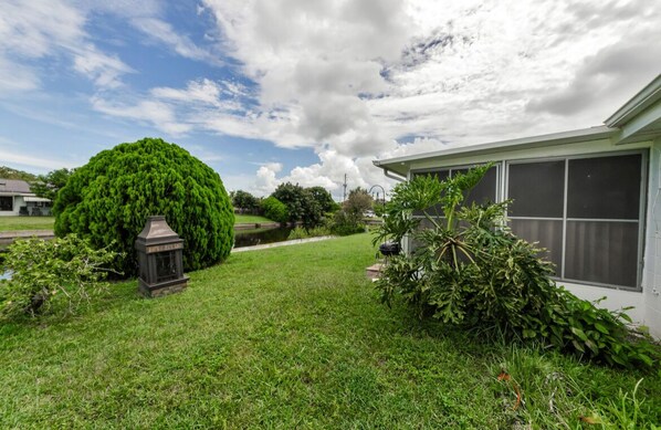A well-maintained lawn with a large tree, a lantern, and a house with a screened window.