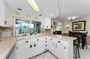A modern kitchen with white cabinetry, a large island, and a view of the outdoors through a glass door. - PROMO 5% weekly and 8% monthly discount!
Psalm139 Canal Front Vacation Home (New Port Richey)