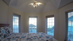 Une chambre à coucher avec un lit, un ventilateur de plafond et trois fenêtres équipées de stores.