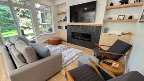 Een moderne woonkamer met een modulaire bank, een open haard, een aan de muur bevestigde televisie en houten planken met decoratieve objecten.