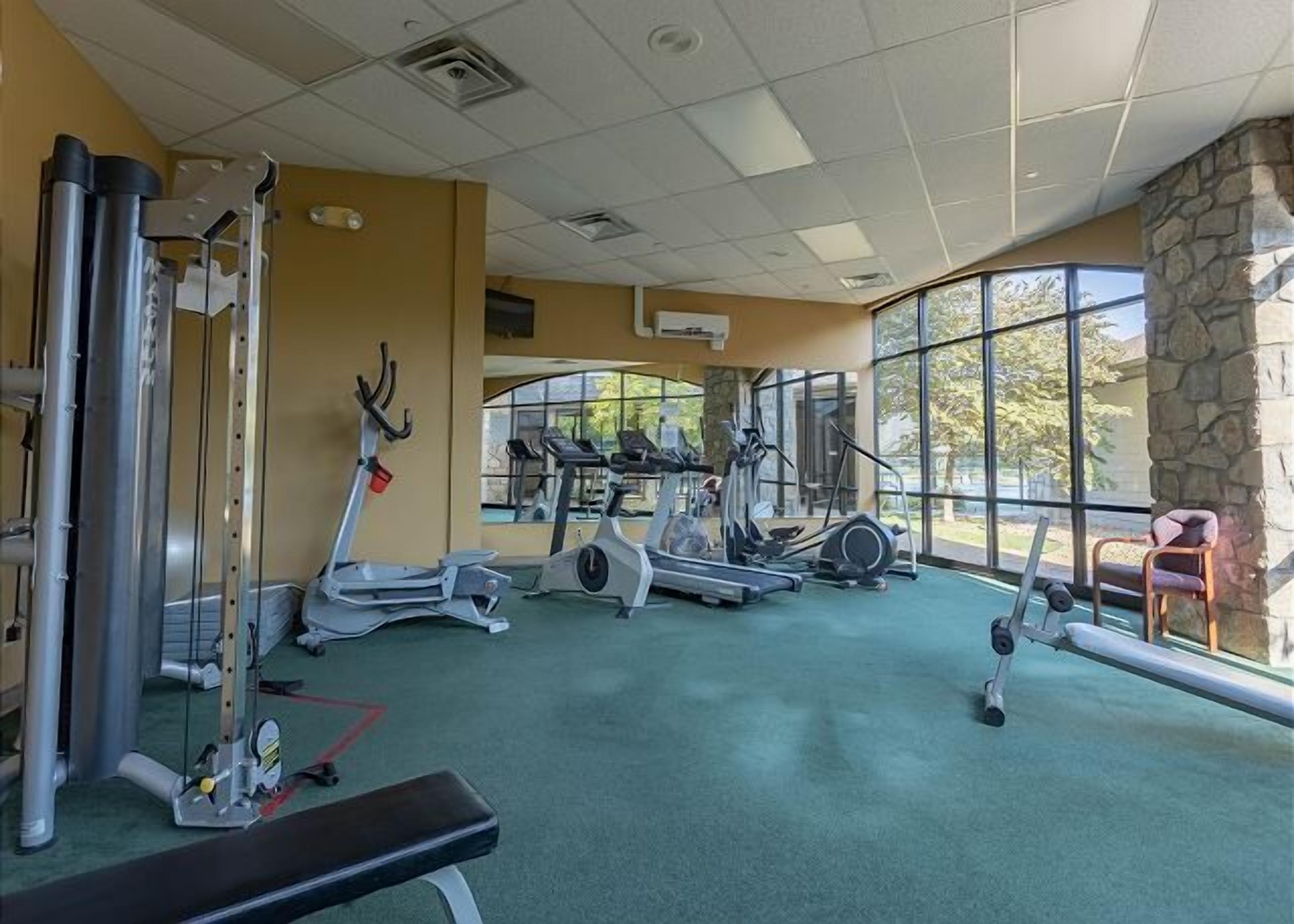 Een fitnessruimte met diverse cardioapparaten, een bank en een stenen muur.