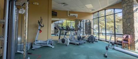 Een fitnessruimte met diverse cardioapparaten, een bank en een stenen muur.