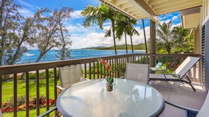 Un balcon avec une table en verre, des chaises et une vue sur l’océan.