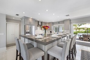 A modern kitchen with a central island, bar stools, and a view of an outdoor pool area.
