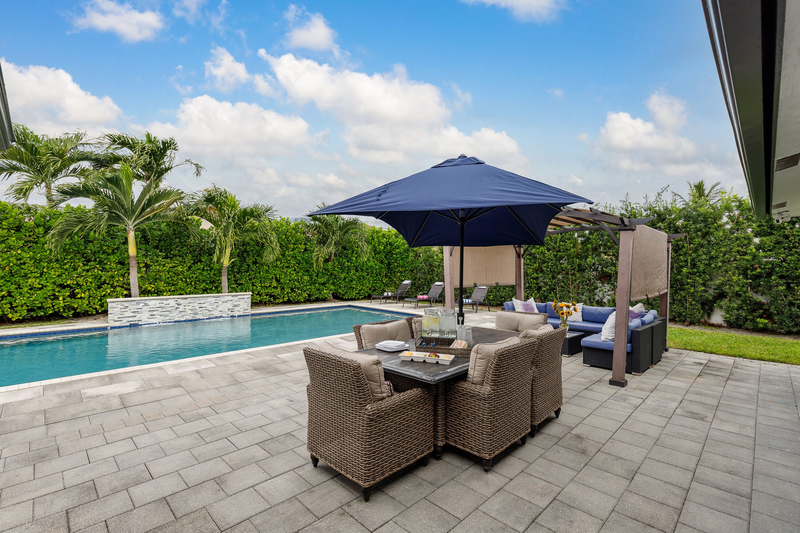 A poolside area with a table and chairs, a large umbrella, and a sofa.