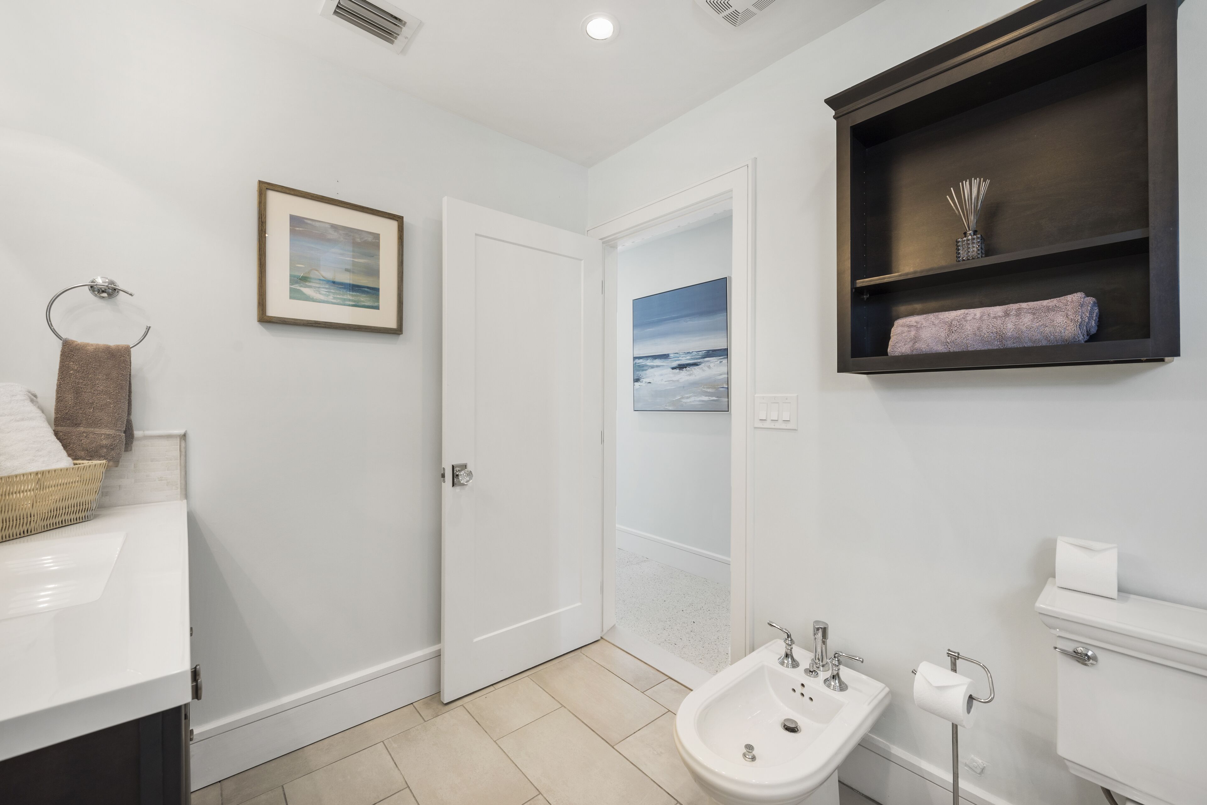 A bathroom with a white sink, a bidet, a toilet, a towel rack, and a framed picture on the wall.