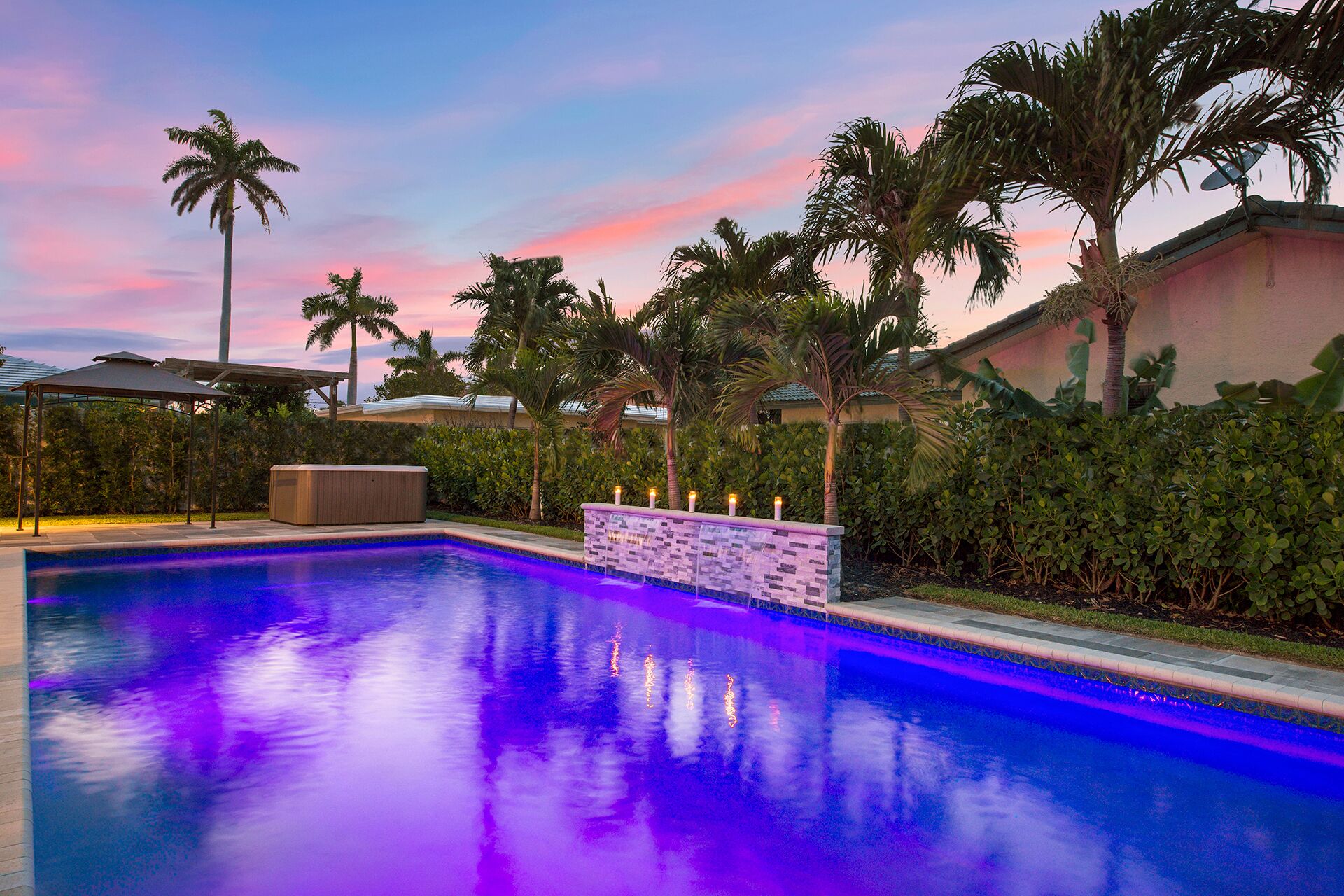A swimming pool with a stone wall and palm trees.