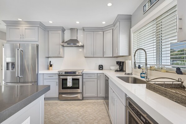 A modern kitchen with stainless steel appliances, white cabinetry, and a large window with blinds.