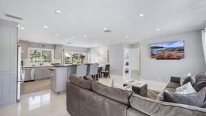 A spacious living area with a large gray sofa, a dining table with chairs, and a kitchen in the background. - SPECIALS!! BEAUTIFUL BEACH HOUSE ! WALK 2 BEACH POOL ! HOT TUB (Lauderdale-By-The-Sea)