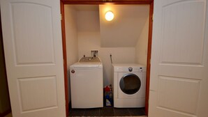 Une buanderie équipée d’un lave-linge et d’un sèche-linge, d’une petite étagère avec une bouteille, et d’un luminaire au plafond.
