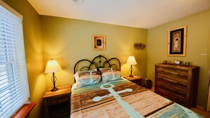 Une chambre à coucher comprenant un lit, deux tables de chevet, une commode et une fenêtre avec des stores.