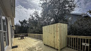 Una terraza de madera con un banco incorporado y una estructura de madera, rodeada de árboles y un cielo nublado.