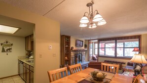 A cozy living room with a fireplace, a dining area with a wooden table and chairs, and a kitchen with wooden cabinets and a built-in oven. - Spacious condo just steps away from main lifts, hot tub, free wifi & parking (Copper Mountain)