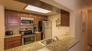 A modern kitchen with granite countertops, stainless steel appliances, wooden cabinets, and a built-in microwave. - Spacious condo just steps away from main lifts, hot tub, free wifi & parking (Copper Mountain)
