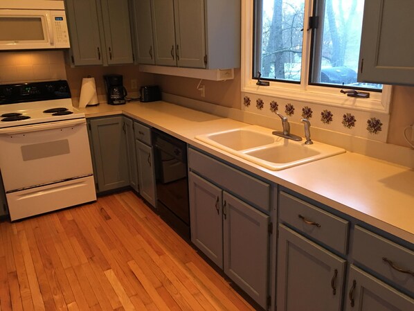 A kitchen with a stove, microwave, sink, and wooden flooring.