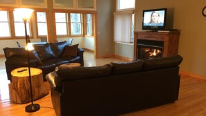 A living room with a black leather sofa, a wooden coffee table, a TV on a wooden stand, and a fireplace.