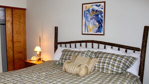 Uma cama com colcha xadrez, cabeceira de madeira e mesa de cabeceira com abajur.