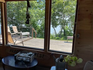 Een houten terras met uitzicht op een meer, een tafel met een mand, en een bordje met de tekst 
