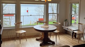 Una habitación con techo de madera, una mesa redonda con sillas, ventanas amplias con vista al agua y un banco junto a la ventana.