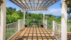 Um deck de madeira com pérgola, guarda-corpos brancos e vasos com plantas.